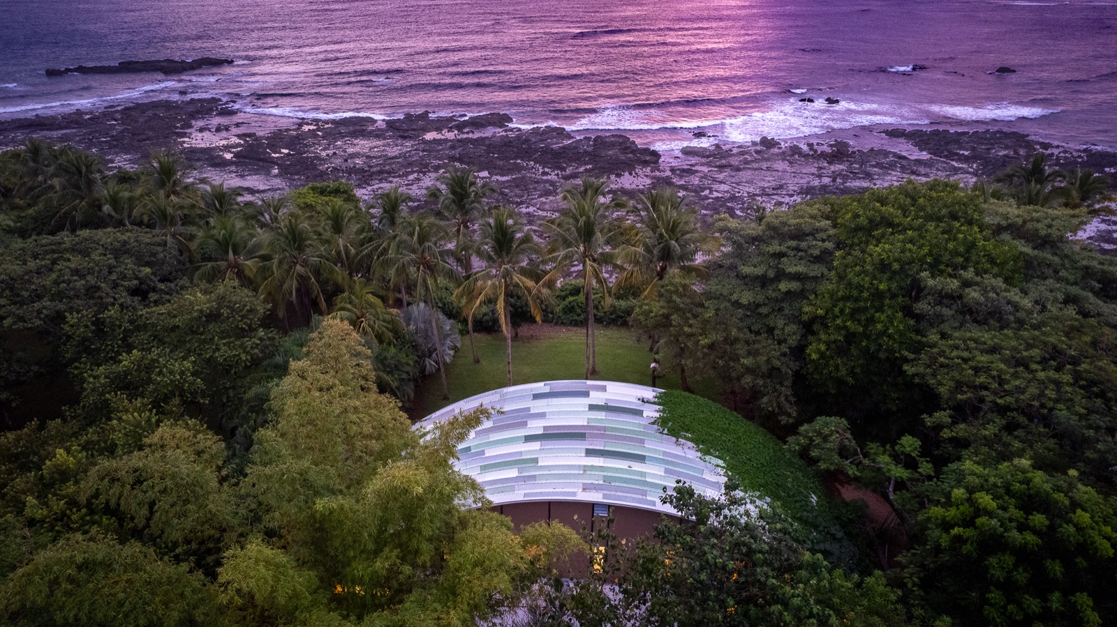 Aerial view of curved modern building by the ocean at sunset